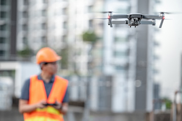 Young Asian engineer man flying drone over construction site. Using unmanned aerial vehicle (UAV)...