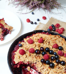 Berry crumble in the black cast-iron frying pan on the white table