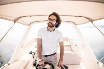Bearded captain of luxury yacht sitting at handwheel , sailing, looking forehead into the sea...
