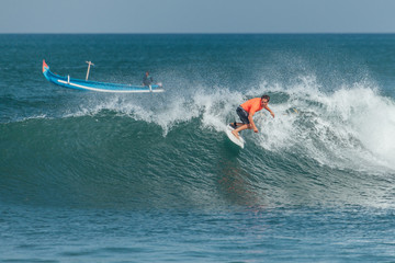 Surfer riding big green wave with fisherman boat in background at Echo beach, Canggu Bali, Indonesia	