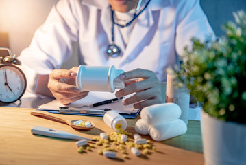 Male Asian doctor holding pill bottle. Doctor working with medicine paperwork clipboard on the desk in hospital clinic. Medical treatment and health care diagnostic concepts.