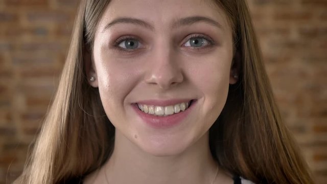 Face of young happy blonda is watching at camera, surprised, brick blurred background