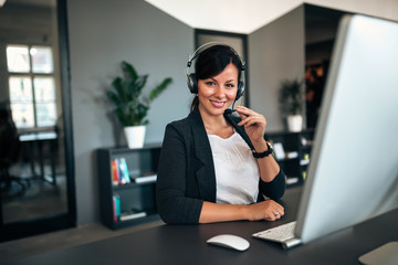 Portrait of beautiful businesswoman working with headset as a customer support, looking at the...