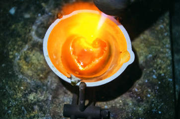  Melted in a crucible precious metal gold or silver in the form of a hot heart. Making of jewelery in the workplace in the workshop of the jeweler.