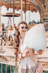 Fototapeta na wymiar Portrait of a Smiling Beautiful Lady in Sunglasses Holding Cotton Candy at Park and Happily Looking in Camera.