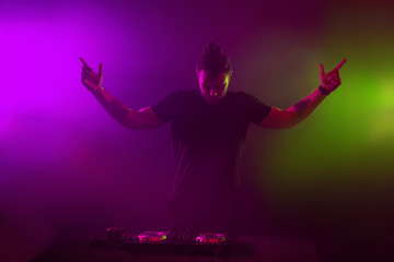 DJ at work mixing sound on her decks at a party or night club with colourful smoke light background