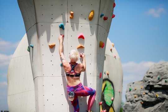 Photo from back of sports girl in leggings on wall for rock climbing against blue sky
