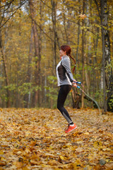 Full-length picture of young brunette jumping with rope at autumn forest