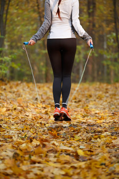 Photo from back of sports girl jumping with rope at autumn forest
