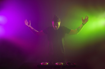 Fototapeta na wymiar DJ at work mixing sound on her decks at a party or night club with colourful smoke light background