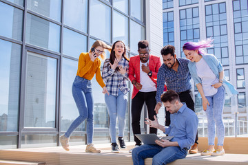 Group of multi ethnic young friends dressed in casual cloth having fun on lounge outdoor area on the roof of office glass building