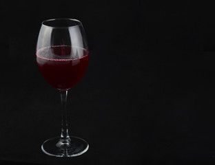 one transparent glass with a red drink on a black background