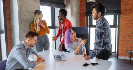Indoor shot of group of multiracial students having meeting at loft studio space background, using laptop and smartphone internet sources trying to write article about their studying at university.