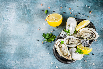 Fresh raw seafood, oysters with lemon and ice on a light blue background