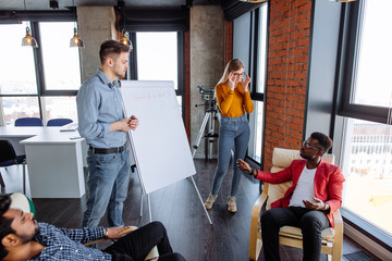 Young dynamic multiracial business team male and female coworkers discussing around a flip chart white board in meeting room