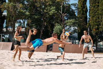 Fit, strong, healthy women and men doing sport on beach. Beach volleyball concept. Two amateur teams have fun playing volleyball on sandy court