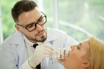 Fototapeta premium Handsome man dentist treats teeth of young woman patient with a mouth mirror and dental excavator .dental checkup at the clinic dentistry attendance