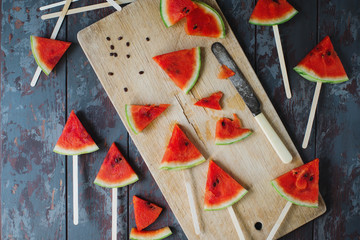 Fresh organic watermelon slice popsicles on rustic wooden board and dark stone background. Selective focus. Tasty summer fruit, healthy lifestyle