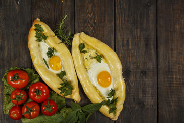 Khachapuri with fresh vegetables caucasian kitchen, close-up on a black wooden table. Adzharian khachapuri. View from above