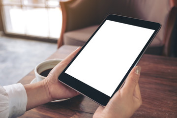 Mockup image of a woman sitting and holding black tablet pc with white blank screen with coffee cup on table