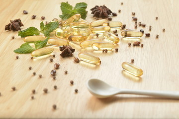 Fototapeta na wymiar Medicine herb, Cod liver oil omega 3 gel capsules with healthy medicinal plant on wooden brown tone background with a white spoon on foreground.