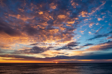 Dramatic sunrise clouds. Very structured and colorful sky. Blue, orange, pink, yellow. Sun rising on horizon about sea. Adventure, clean, sail, free, quiet, relax, holiday.