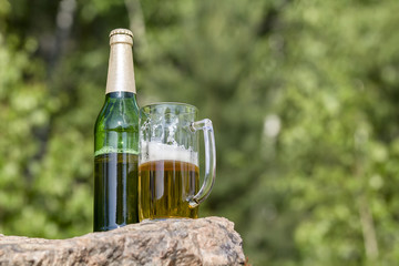 Bottle and mug of beer stands on a rock in the forest