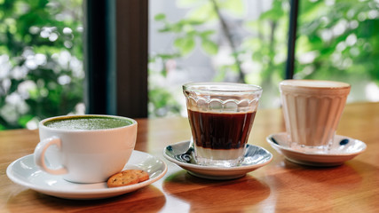 Green tea latte, Vietnamese coffee and latte served on wooden table with blur trees in background