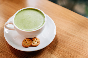 Hot and smooth green tea latte with froth served in white ceramic cup with biscuits