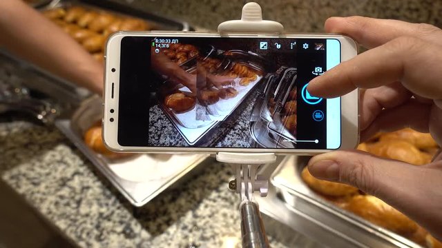 A man's hand holds a smartphone and makes photos of sweets. The concept of food photo for social networks. Buffet Restaurant.