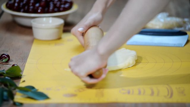Woman hands roll out the dough on the kitchen table to make a pie with berries.