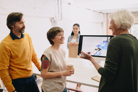 Group of modern creative people chatting cheerfully standing against computer screen with abstract painting in design studio, copy space