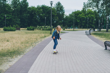 cute little child in denim clothing skating on skateboard in park