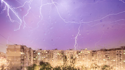 Lightning storm over city in purple light, the view from the window