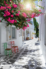 Gasse mit bunten Bougainvillea Blumen, weißen Häusern und farbigen Stühlen in Parikia, Paros,...