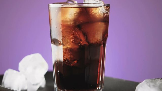 Cola with ice cubes and bubbles in glass, slow motion.