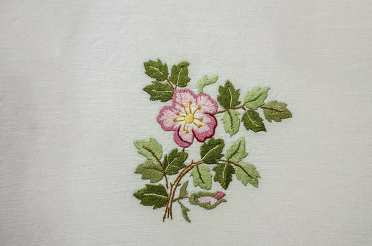 Embroidered satin stitch in pink shades, tea rose  with bud and leaves on coarse cotton fabric

