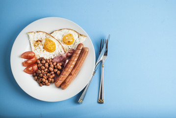 Plate of breakfast with fried eggs, bacon beans tomatoe slices isolated on blue background