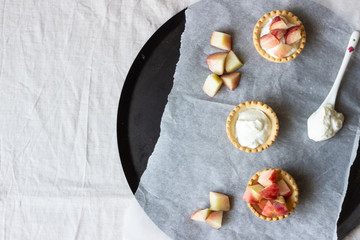 Obraz na płótnie Canvas Homemade mini tartlets with cream and fresh peaches on light grey background.