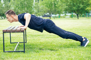 handsome young man in a black T-shirt pushups on a park bench