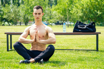 A handsome young man without a T-shirt is engaged in yoga and Pilates in the park. Exercise outdoors