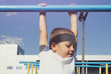 Fototapeta premium The boy is hanging on the crossbar in the summer on the playground. Close-up