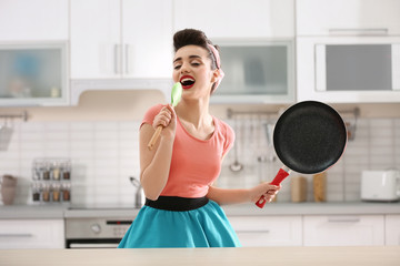 Funny young housewife using spoon as microphone in kitchen
