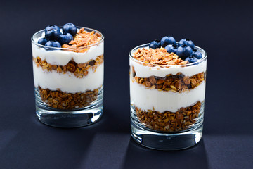 Homemade baked granola with yogurt and blueberries in a glass on a black background. Space for text or design.