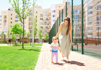 Woman supporting her baby daughter while she learning to walk outdoors