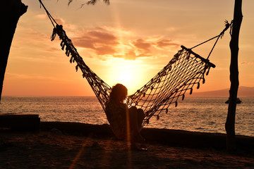 Siilhouette of woman sitting in hammock at sunrise on the beach, Gili Meno Island, Lombok, Indonesia