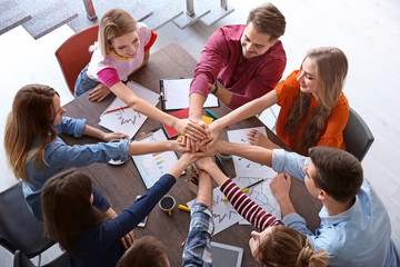 Young people putting hands together while working on project indoors. Unity concept
