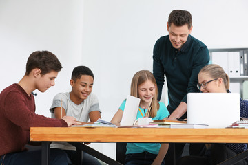Group of teenagers doing homework with teacher in classroom