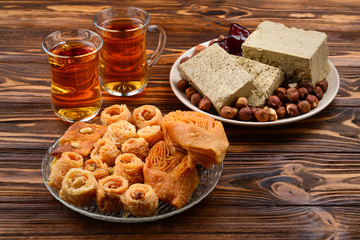 Assorted traditional eastern desserts with tea on wooden background. Arabian sweets on wooden table. Baklava, halva, rahat lokum, sherbet, nuts, dates, kadayif on plates. Space for text.