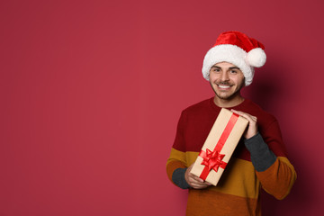 Young man with Christmas gift on color background